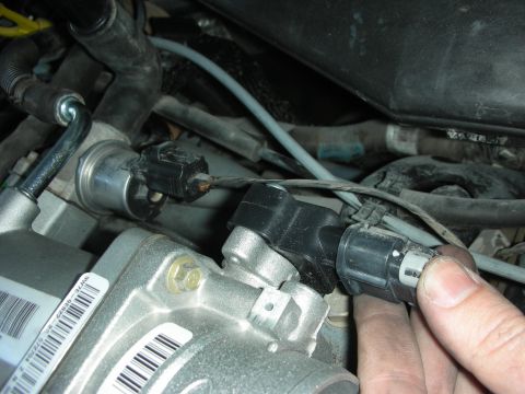 2004 Ford Crown Victoria - A hand disconnects a sensor from an engine component, showing intricate mechanical parts.