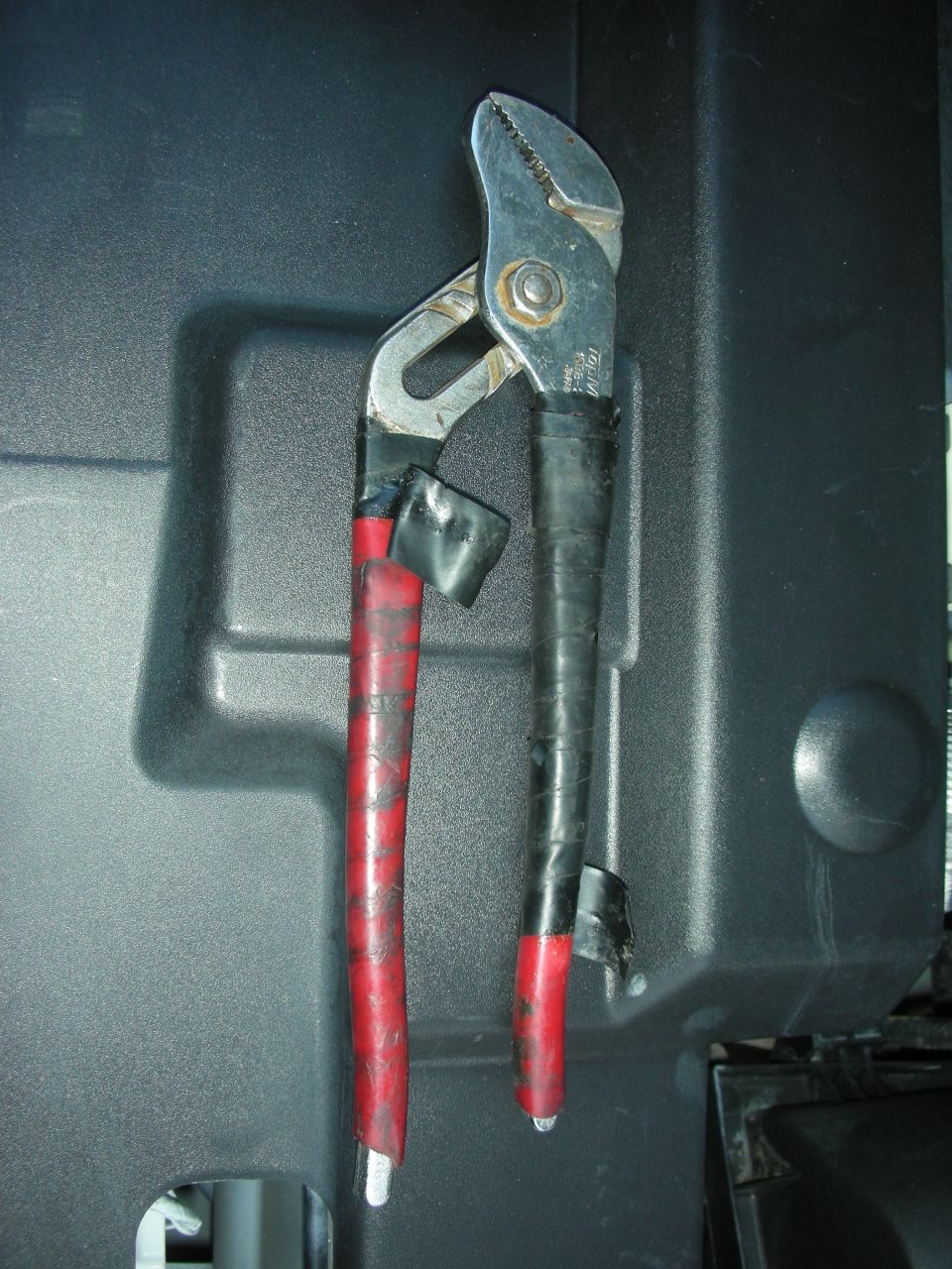 Channel lock pliers with red and black tape on handles, resting on a black plastic surface