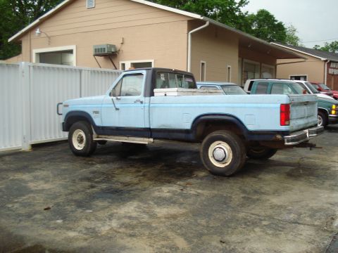 1967 Ford F-250 - A light blue pickup truck is parked outside a building, with other vehicles visible in the background.