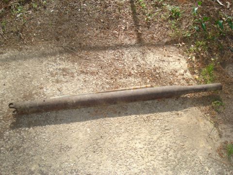 1967 Ford F-250 - A rusty exhaust pipe is shown lying on the ground, with vegetation in the background.