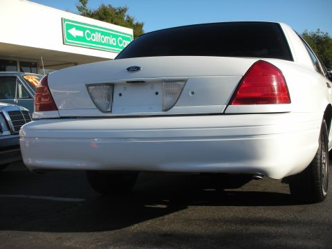 2004 Ford Crown Victoria - Rear view of a white 2004 Ford Crown Victoria parked in front of a building with a green sign.