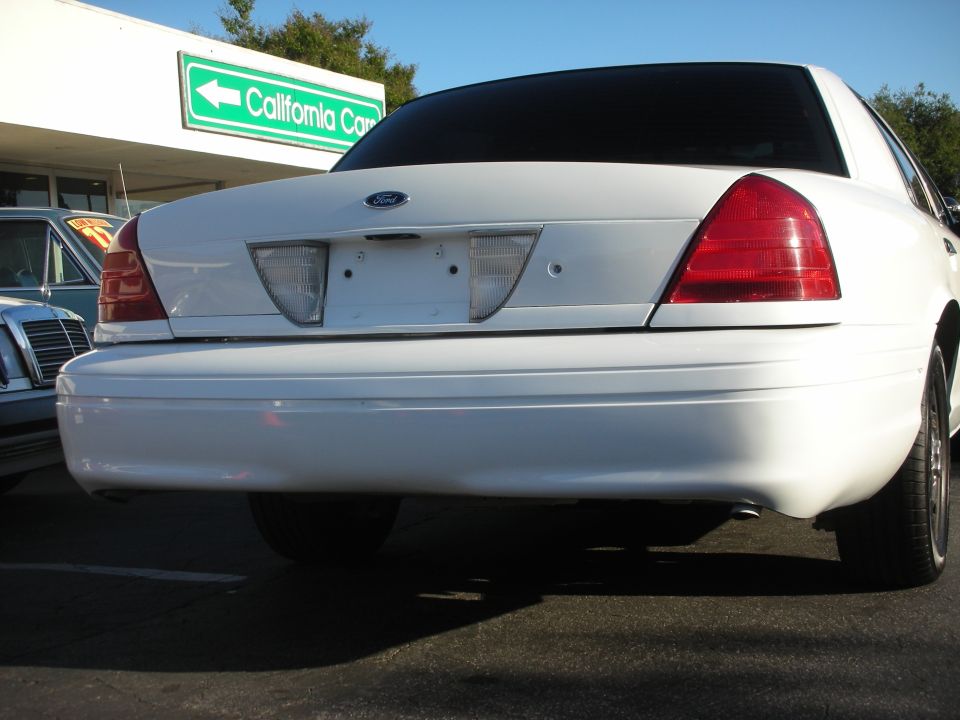 White 2004 Ford Crown Victoria rear view. Another car is visible to the left
