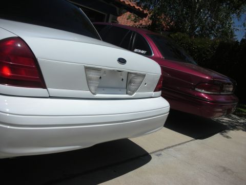 2004 Ford Crown Victoria - Two Ford Crown Victorias, one white and one maroon, are parked side-by-side in a driveway.