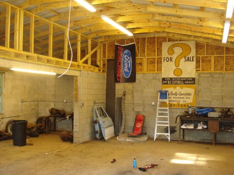1967 Ford F-250 - A cluttered garage scene displays automotive parts, tools, and promotional signs, suggesting a workshop or storage area.