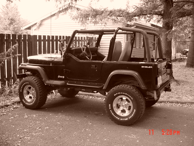 Black Jeep Wrangler parked on asphalt driveway, side view