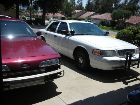 2004 Ford Crown Victoria - A white police car is parked next to a maroon car in a driveway.