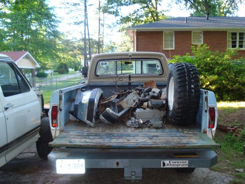 1967 Ford F-250 - A light blue Ford pickup truck, likely from the mid-1970s, is seen from the rear with its bed full of engine components and a spare tire.