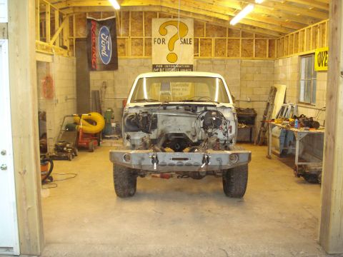 1967 Ford F-250 - A white Ford truck chassis, possibly from the 1980s, sits disassembled in a workshop with tools and equipment around.