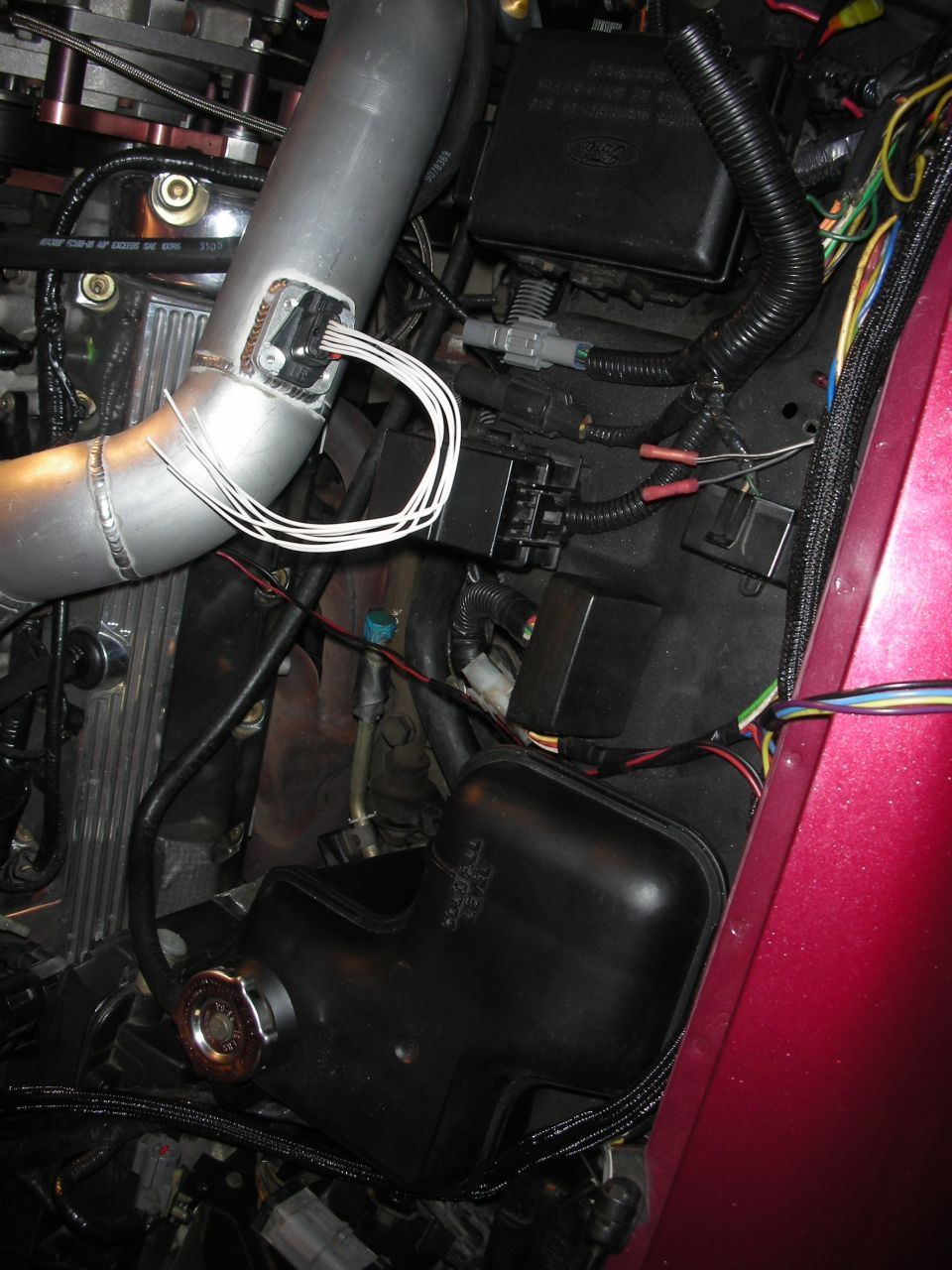 Engine bay with custom intercooler piping and lots of wiring. Shows fuse box and other engine components