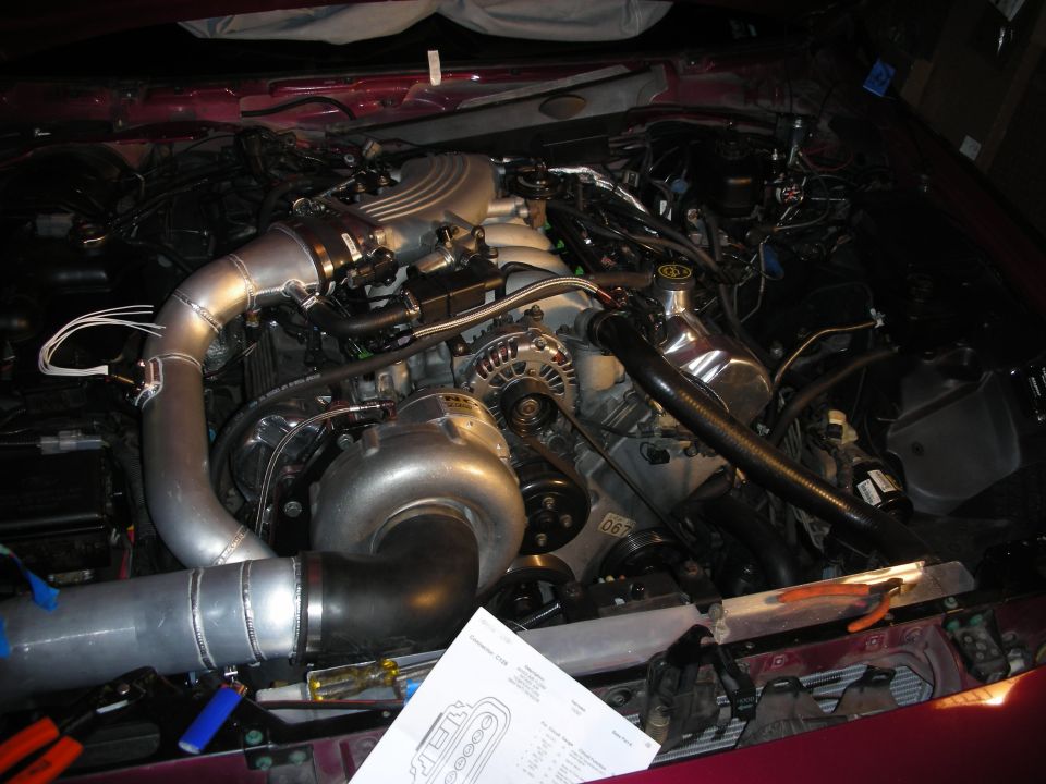Engine bay with large turbocharger and custom piping installed. Some wiring and tools are visible