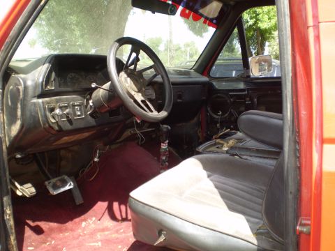 1969 Ford F-250 - The interior of a truck shows a worn dashboard, aftermarket steering wheel, and ripped seats, with exposed wiring and pedals.