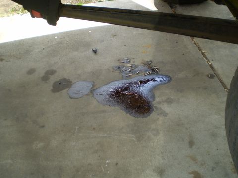 1969 Ford F-250 - A puddle of oil and debris on a concrete surface, with a portion of a vehicle's frame visible overhead.