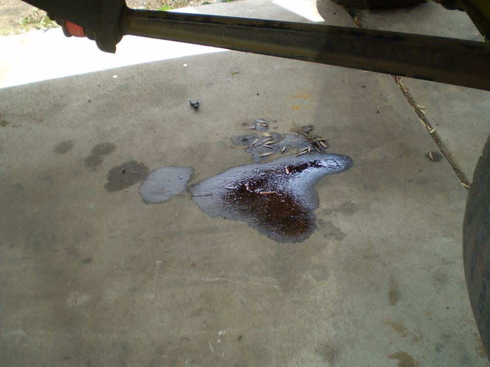 Oil spill on concrete with debris, part of a vehicle frame above