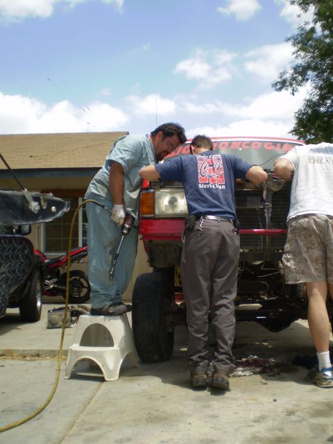 1969 Ford F-250 - Three men are gathered around the front of a red truck, appearing to be working on it. One man is on a stool with a tool.