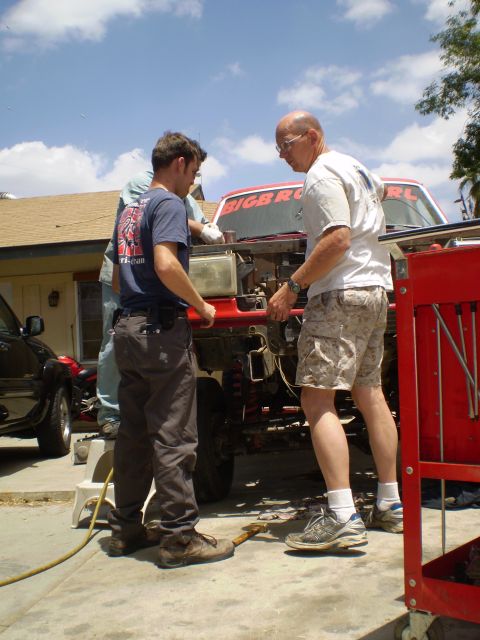 1969 Ford F-250 - Men are working on a vehicle part in a sunny outdoor setting.