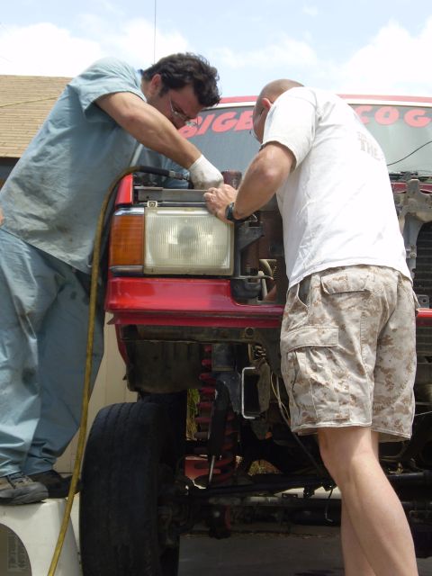 1969 Ford F-250 - Two men are working on the front end of a red truck, with the Supermotors.net logo visible at the bottom.