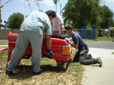 1969 Ford F-250 - Men are working on the red bed of a truck, likely a Ford F-Series from the 1980s.