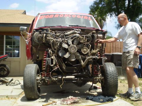 1969 Ford F-250 - A man inspects the exposed engine bay of a red truck, with its front end partially dismantled.