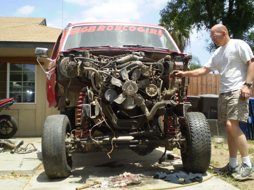 Man looking at red truck with engine removed, front end disassembled