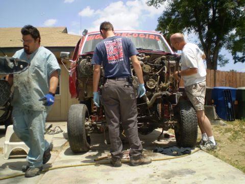 1969 Ford F-250 - Three men work on the exposed engine bay of a red truck chassis.