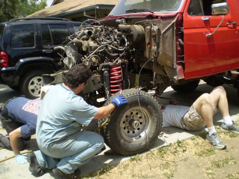 1969 Ford F-250 - Mechanics work on a disassembled red truck, with a black SUV in the background.