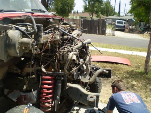1969 Ford F-250 - A person works on the complex engine and suspension of a red truck with its hood removed.