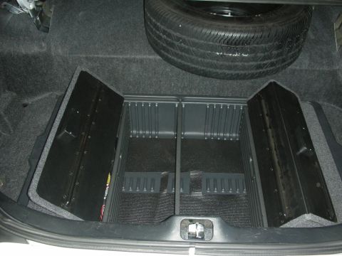 2004 Ford Crown Victoria - Sedan trunk interior with gray carpet, an upright full-size spare and molded black divided storage trays.