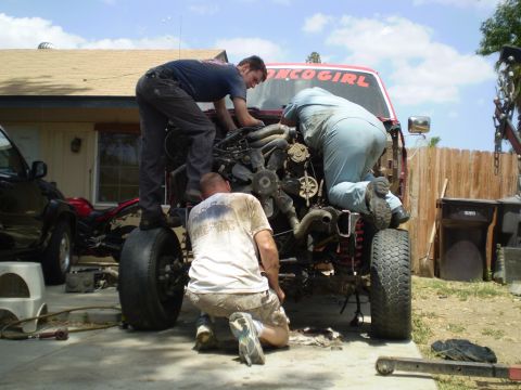 1969 Ford F-250 - Mechanics work on the engine of a red truck labeled "BRONCO GIRL" in a driveway.
