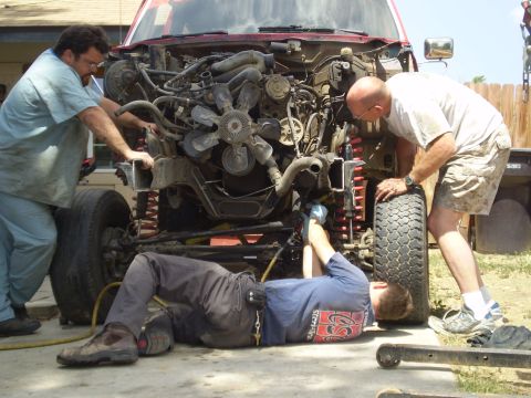 1969 Ford F-250 - A team of mechanics is actively engaged in servicing the engine compartment of a red truck, with one person lying on the ground.