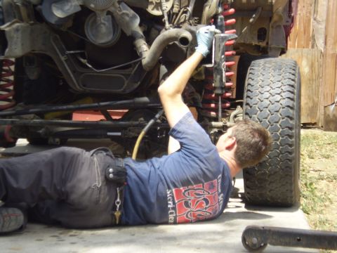 1969 Ford F-250 - A mechanic works on the engine and suspension of a vehicle, with a large tire visible.