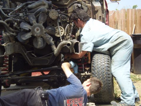 1969 Ford F-250 - Two individuals are actively working on the complex engine of a vehicle, with a large tire in the foreground.