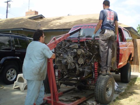 1969 Ford F-250 - Two men use an engine hoist to remove the engine from a red SUV in a driveway.