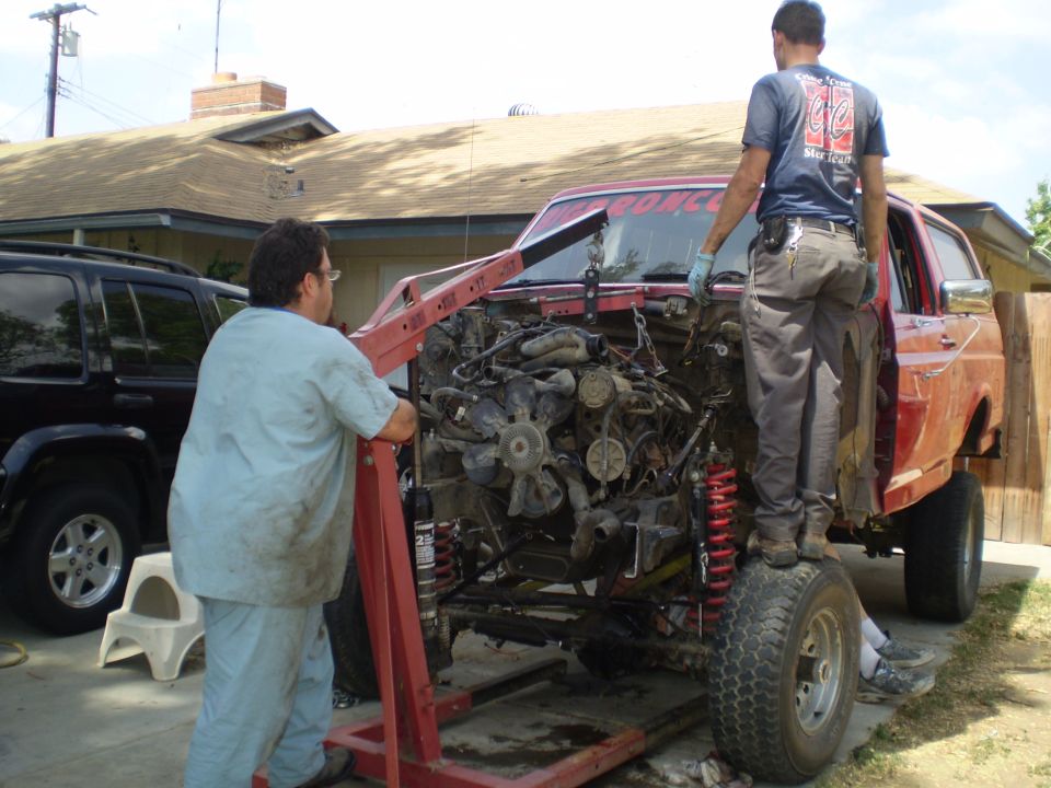 Engine being removed from a red SUV with an engine hoist; black SUV parked nearby