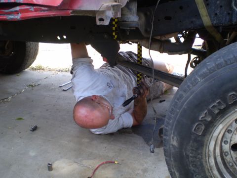 1969 Ford F-250 - Mechanic performs maintenance on a vehicle's undercarriage, with tools scattered on the concrete floor.