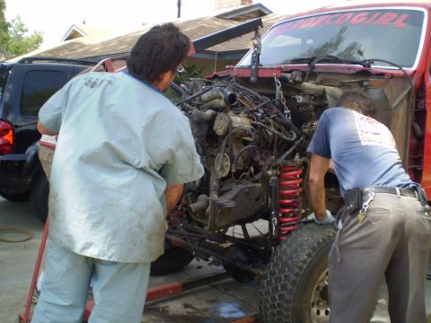 1969 Ford F-250 - Mechanics are in the process of removing the engine from a red truck, with a black SUV visible in the background.