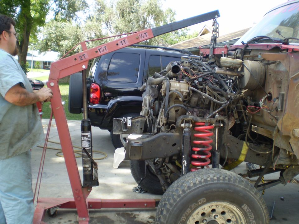 Engine being removed from a truck with a cherry picker, black SUV in background