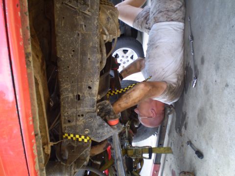 1969 Ford F-250 - A mechanic works on the underside of a vehicle, with tools scattered on the ground nearby.