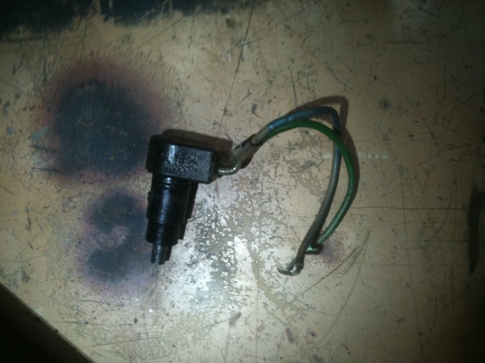 Small black automotive switch or sensor with green and gray wire pigtail on a workbench