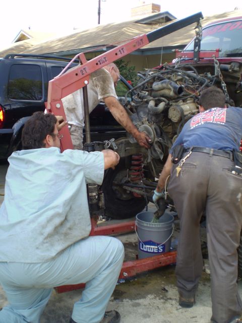 1969 Ford F-250 - Mechanics work on removing an engine with a red engine hoist, while a black SUV is parked nearby.