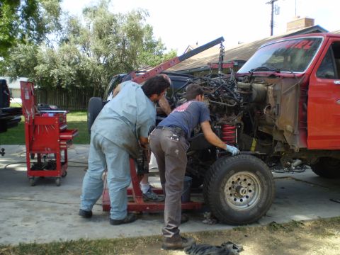 1969 Ford F-250 - Mechanics work on removing the engine from a red truck using an engine hoist.