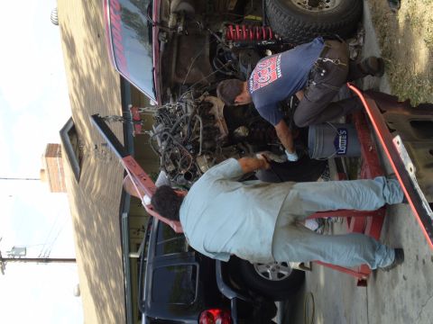 1969 Ford F-250 - Mechanics use an engine hoist to remove the motor from a truck, with a dark SUV nearby.