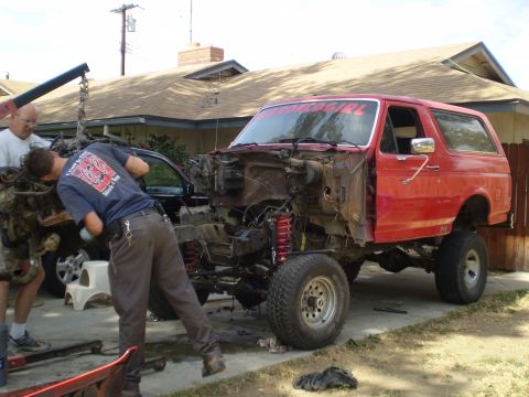 1969 Ford F-250 - Two men and a crane work on the engine of a red SUV in a driveway.