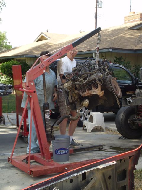 1969 Ford F-250 - Two men use an engine hoist to remove the engine from a dark-colored truck.