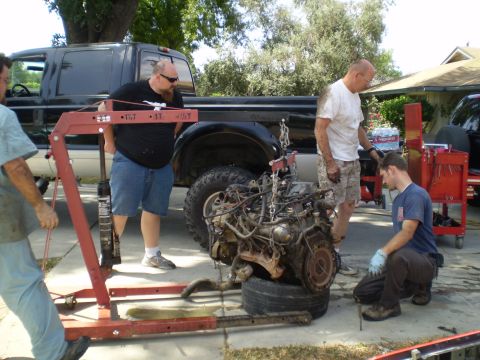 1969 Ford F-250 - Men work on removing an engine from a black Ford F-Series truck using an engine hoist.