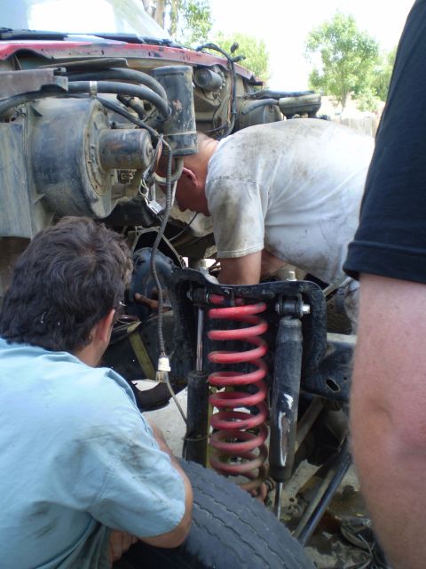 1969 Ford F-250 - Mechanics are seen working on the front suspension of a red truck, focusing on the coil springs and shock absorbers.