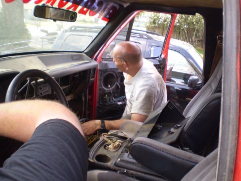 1969 Ford F-250 - Interior view of a red truck with a man working on the dashboard, with other vehicles visible through the open door.