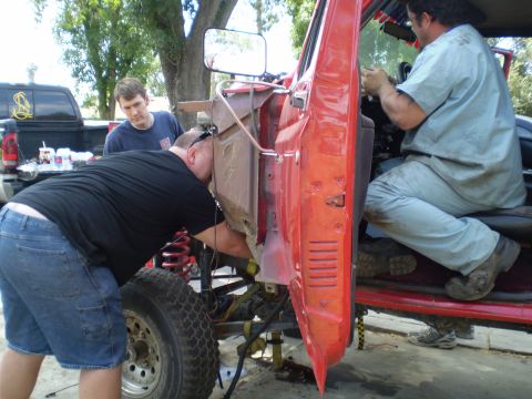 1969 Ford F-250 - Men are working on the engine of a red truck, with another truck in the background.
