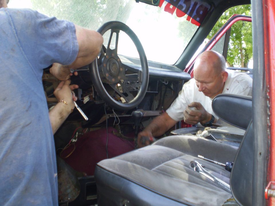 Interior of a red truck with men working on the dashboard and steering column
