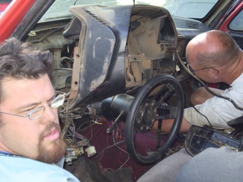 1969 Ford F-250 - Two men work on the exposed wiring of a vehicle's dashboard, with the red exterior visible.