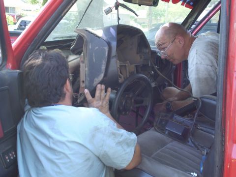 1969 Ford F-250 - Two men are working on the interior of a red vehicle, focusing on the dashboard area.